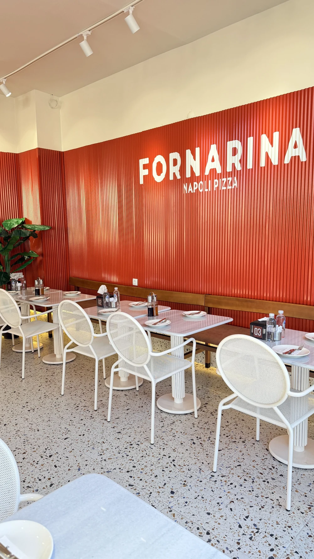 Fornarina yazılı kırmızı duvarın önünde restoran masaları